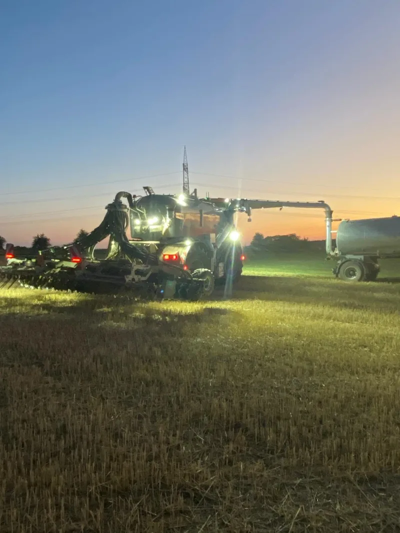 Gülletechnik mit eingeschalteten Arbeitsscheinwerfern bei der Ausbringung in der Abenddämmerung